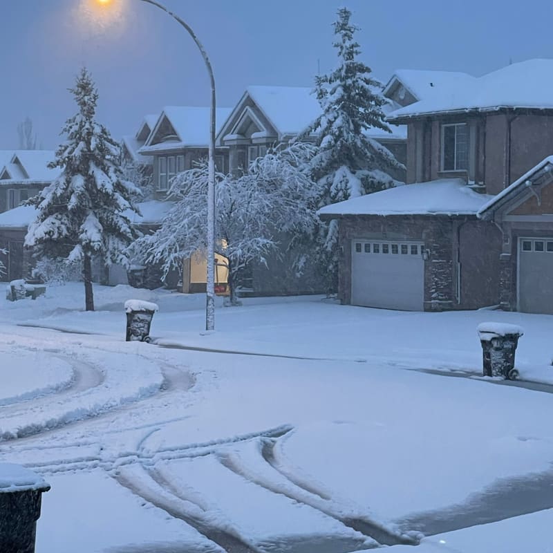 Snow-covered residential street with houses and streetlights at dusk in Calgary