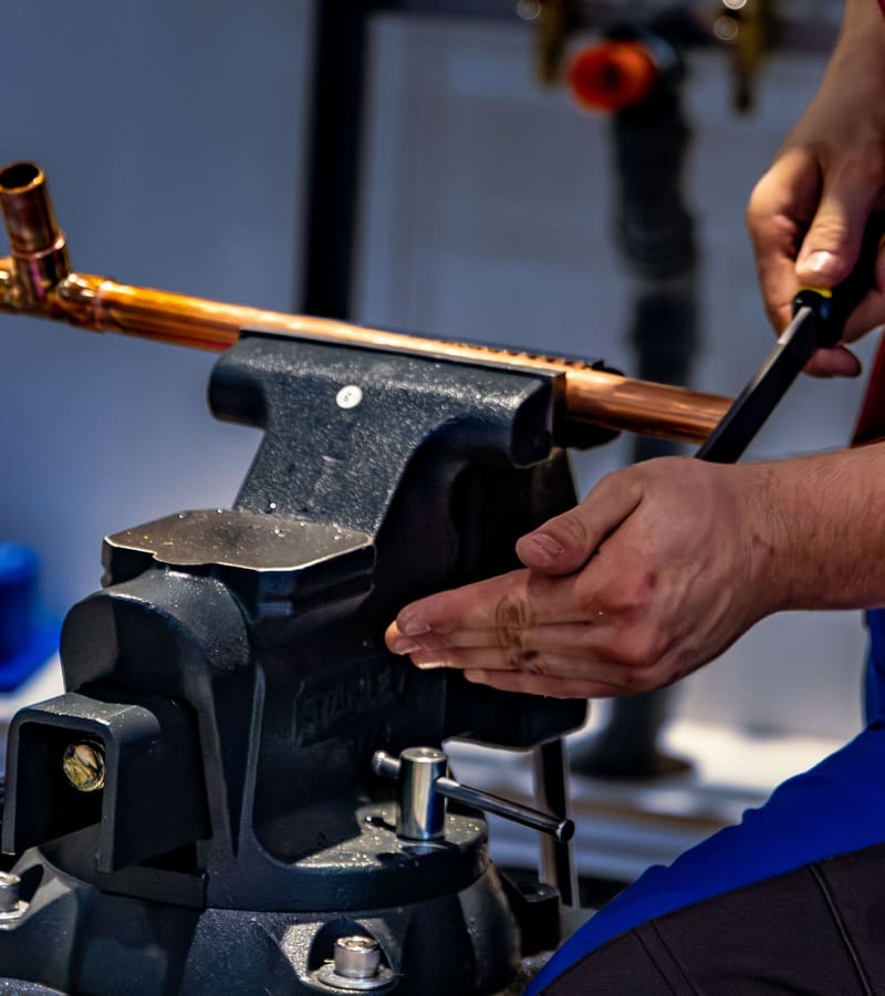 Plumber bending a copper pipe with a pipe bender clamped in a vise