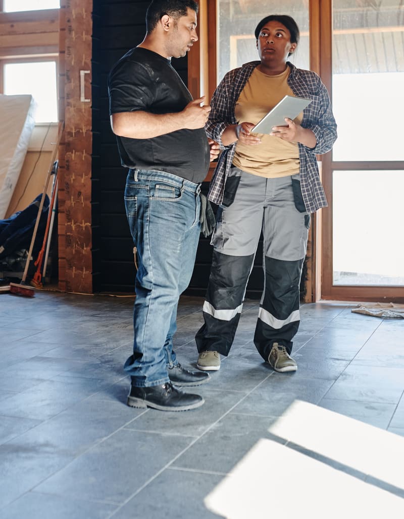 Two contractors talking over plans inside a house under renovation