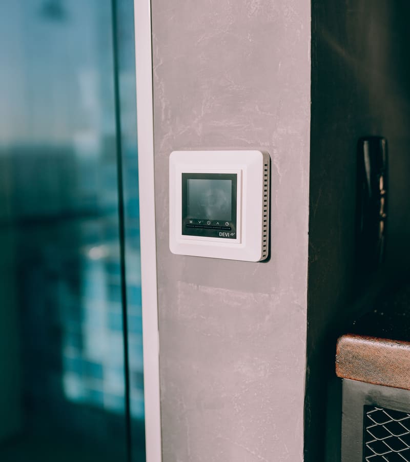 Digital thermostat mounted on a wall next to a window