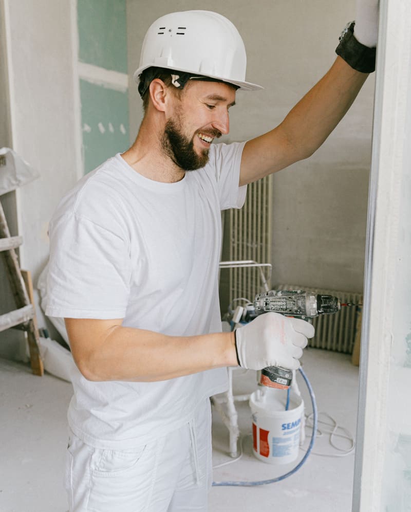Smiling tradesman in a hard hat using a paint sprayer during an indoor renovation
